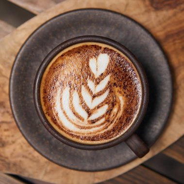 Kremalı kahveyle dolu güzel, kahverengimsi, sıcak bir kahve fincanı. Kahveli, ahşap bir kahve dükkanında servis ediliyor. Organik adil ticaret kahvesi yukarıdan çekilmiş.