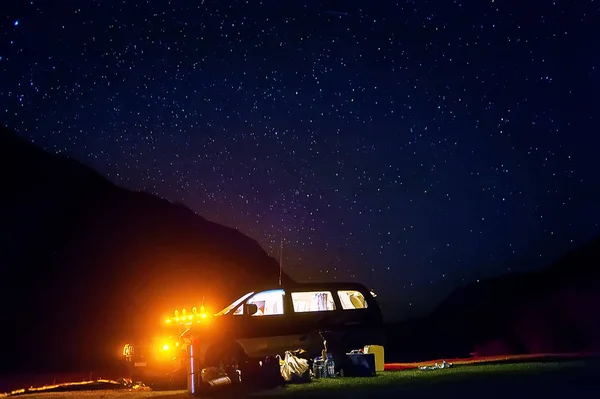 Camping with tents and car under the stars. Night camping. Romantic couple tourists have a rest at a campfire under amazing night sky full of stars and milky way. Astrophotography.