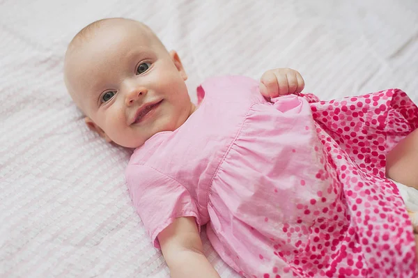 A rózsaszín ruha aranyos kislány fekszik fehér háttere. Közeli kép: portré, mosolygós baba — Stock Fotó
