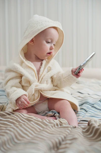 Bébé drôle mignon en peignoir avec téléphone dans ses mains — Photo