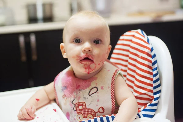 Kisgyermek lány eszik levest, etetőszék, fröccsen körül magát. Játék az élelmiszer- és tanulás enni koncepció. Piszkos arc boldog gyerek. A baba eszik egy foltos arc portréja. — Stock Fotó