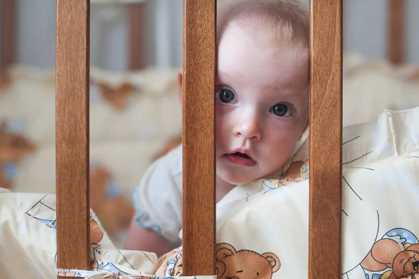 Aranyos mosolygós baba keresi ki a kéró. Vicces gyerek az ágyban. Közelről portré — Stock Fotó
