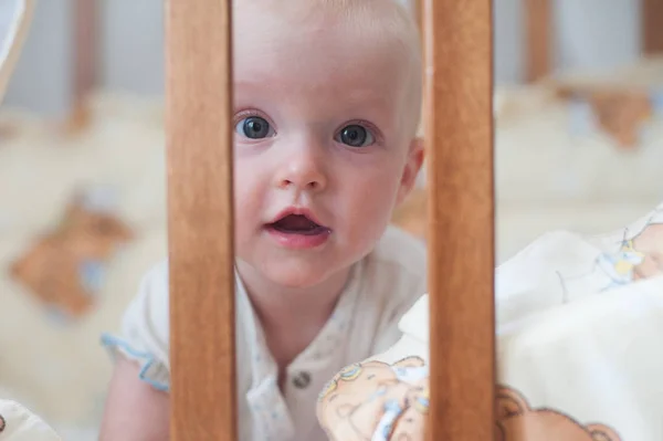Aranyos mosolygós baba keresi ki a kéró. Vicces gyerek az ágyban. Közelről portré — Stock Fotó