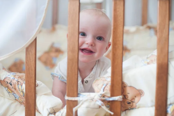 Lindo bebé sonriente mirando desde la cuna. Chico divertido en la cama . — Foto de Stock