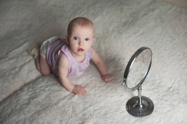 Baba lány llying ágyra, és nézi a tükörképét a tükörben. — Stock Fotó