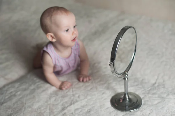 Bambina che si sdraia sul letto e guarda il suo riflesso nello specchio . — Foto Stock