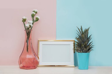 Modern ev dekorasyonu ile altın boş fotoğraf çerçevesi, vazo ve tropikal bitki pembe mavi zemin üzerine sahte
