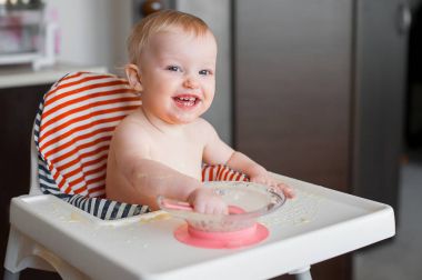 Yüksek sandalyede oturan ve kendini kaşıkla yemeye öğrenme küçük şirin kız. Komik gülen mutlu bebek leke gıda tablo