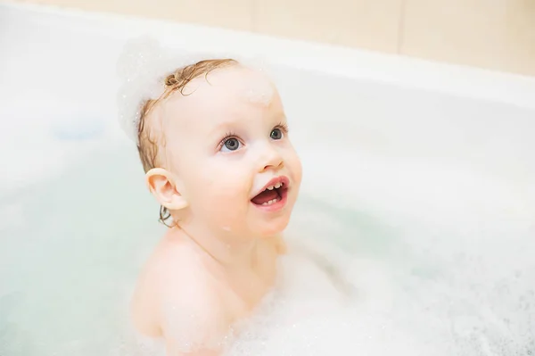 Boldog aranyos kislány a fürdőszobában. Mosolygó gyerek játszik a hab és a kacsa — Stock Fotó