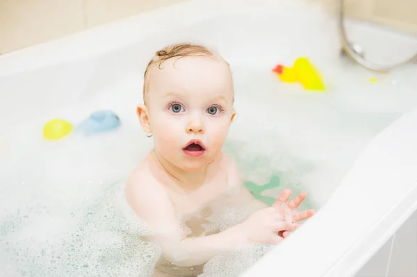 Feliz bonito bebê menina no banheiro. Criança sorridente brincando com espuma e pato — Fotografia de Stock