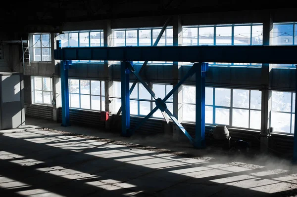 Manufacturing factory. Empty hangar building. Blue toned background. The production room with large windows and metal structures