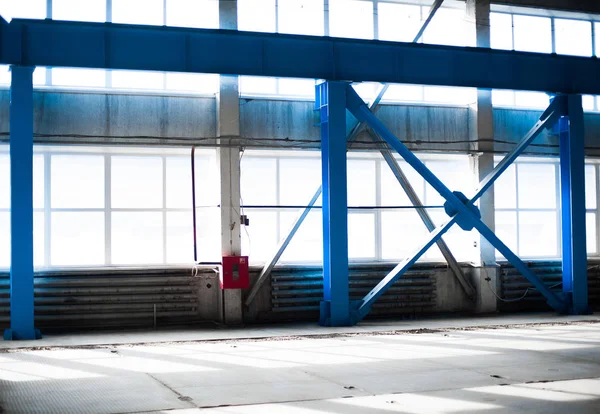 Manufacturing factory. Empty hangar building. Blue toned background. The production room with large windows and metal structures