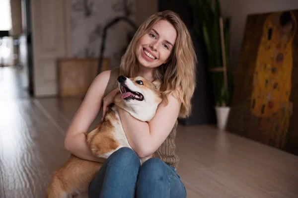 Улыбающаяся девушка играет со своей валлийской Корги Пемброк щенок, счастливый милый пес. Собака лежит на руках своих хозяев — стоковое фото