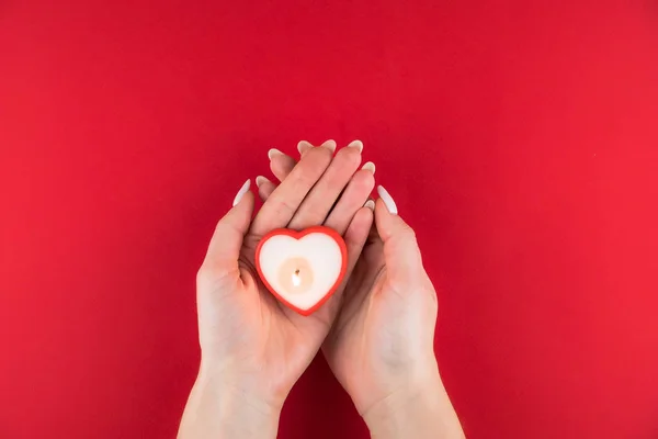 Vela na forma de um coração nas mãos de uma mulher no fundo vermelho para o dia dos namorados . — Fotografia de Stock