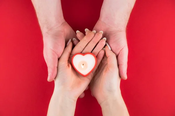 Vela na forma de um coração nas mãos de um casal no fundo vermelho para o dia dos namorados — Fotografia de Stock