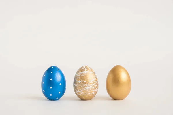 Tres huevos dorados de Pascua sobre fondo azul. Mínimo concepto de Pascua. Tarjeta de Pascua feliz con espacio de copia para el texto. Vista superior, plano — Foto de Stock