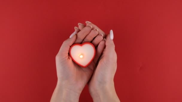 バレンタインデーのための赤い背景にカップルの手の中に心の形でろうそくを燃やす — ストック動画