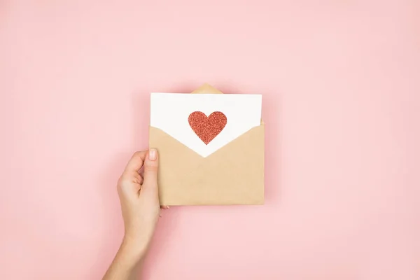 Lettre d'amour entre les mains des femmes le jour de la Saint-Valentin. Carte postale à la main avec coeur rouge sur fond rose. 14 février concept — Photo
