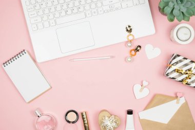 Pembe arka planda ofis aksesuarları olan kadın ofis masası. Kadın çalışma alanı sulu, mum ve kozmetik ile.