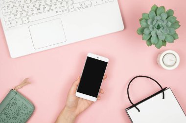 İnternetten Alışveriş Konsepti. Pembe arka planda telefonu ve laptopu olan kadın elleri. Üst görünüm, alanı kopyala.