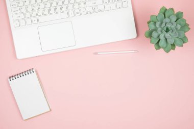 Ev ofisinin masası düzdü. Dizüstü bilgisayarı, defteri, pembe arka planda kalemi olan kadın çalışma alanı. Üst görünüm kadınsı arkaplan. 