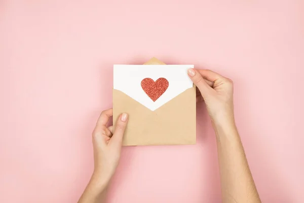 Lettre d'amour entre les mains des femmes le jour de la Saint-Valentin. Carte postale à la main avec coeur rouge sur fond rose. 14 février concept — Photo