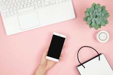 İnternetten Alışveriş Konsepti. Pembe arka planda telefonu ve laptopu olan kadın elleri. Üst görünüm, alanı kopyala.