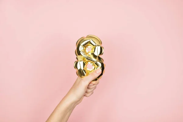 Goldfolien-Luftballons mit der Zahl 8 in weiblicher Hand auf rosa Hintergrund. Glücklicher Frauentag — Stockfoto