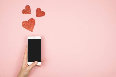 Sevgililer Günü konsepti, ekranda cep telefonu ve pembe arka planda kırmızı kalpler. Sosyal medyada aşk
