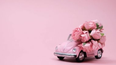 Pembe retro oyuncak araba pembe arka planda gül buketi getiriyor. 14 Şubat kartı, Sevgililer Günü. 8 Mart, Uluslararası Mutlu Kadın Günü