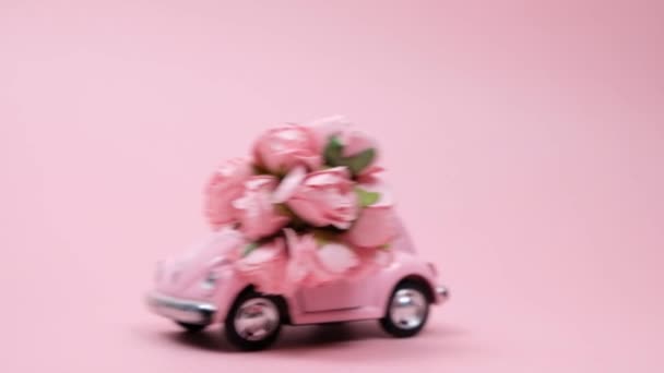 Roze retro speelgoedauto leveren boeket rozen op roze achtergrond. 14 februari kaart, Valentijnsdag. 8 maart, Internationale Gelukkige Vrouwendag — Stockvideo