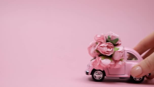 Pembe arka planda gül buketi olan pembe retro oyuncak arabayı iten bir kadın. 14 Şubat kartı, Sevgililer Günü. 8 Mart, Uluslararası Mutlu Kadın Günü — Stok video
