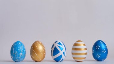 Yumurtalar beyaz masada yuvarlanıyor, birbirlerine vuruyorlar. Beyaz arka planda izole edilmiş Paskalya altınlı yumurtalar. Asgari paskalya konsepti. Mutlu Paskalyalar.