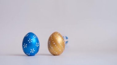 Yumurtalar beyaz masada yuvarlanıyor, birbirlerine vuruyorlar. Beyaz arka planda izole edilmiş Paskalya altınlı yumurtalar. Asgari paskalya konsepti. Mutlu Paskalyalar.