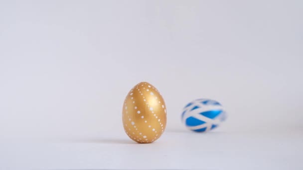 卵は白いテーブルの上を転がって、お互いにノックしている。白い背景に隔離されたイースターゴールドの装飾卵。最小限のイースターコンセプト。ハッピーイースターカード. — ストック動画