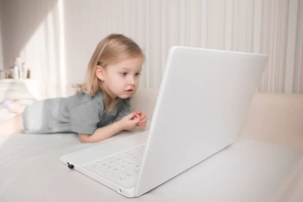 Carino piccola ragazza bionda utilizzando computer portatile guardare cartoni animati divertenti a casa . — Foto Stock