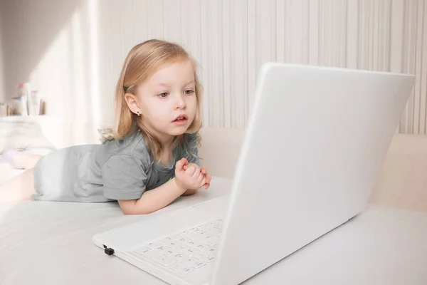 Aranyos kis szőke lány használ laptop nézni vicces rajzfilmek otthon. — Stock Fotó