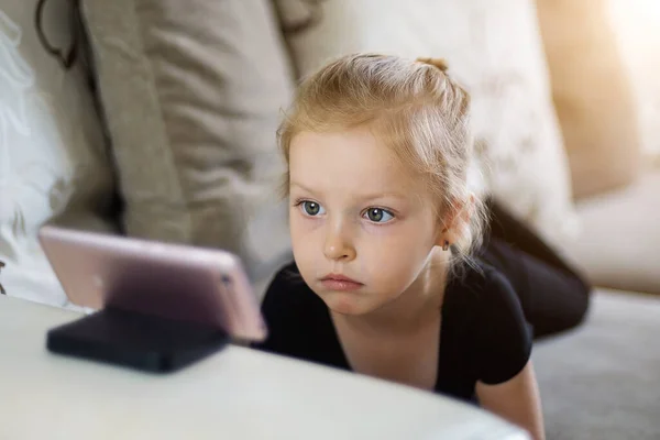 Távolságtanulás, online oktatás gyerekeknek. A kislány otthon tanul az okostelefon előtt. Gyermek néz online rajzfilmek, gyerekek számítógépes függőség, szülői felügyelet koncepció. — Stock Fotó