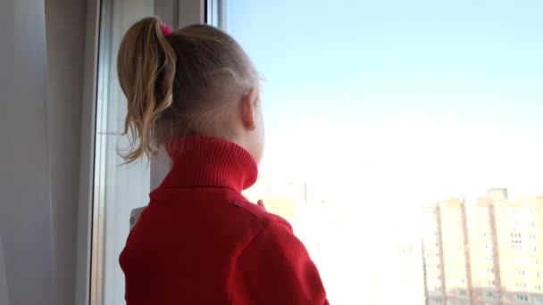 Niña triste mirando por la ventana. Quédate en cuarentena en casa. Concepto de aislamiento. Brote epidémico de virus, crisis médica sanitaria — Vídeo de stock