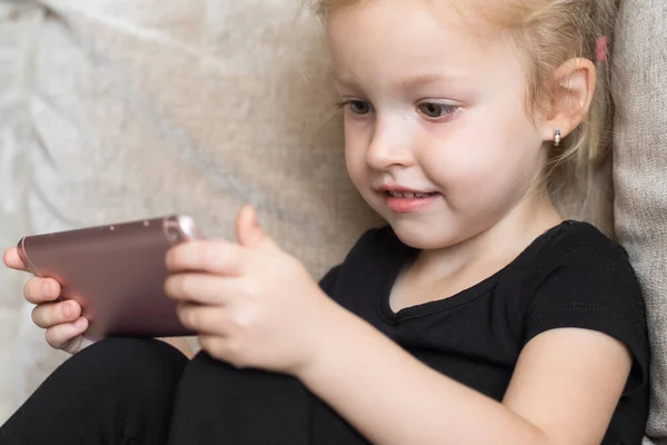 Apprendimento a distanza, educazione online per bambini. Ragazza felice tenendo smartphone in mano. Bambino che guarda cartoni animati online, bambini dipendenza dal computer, controllo parentale. Quarantena a casa — Foto Stock