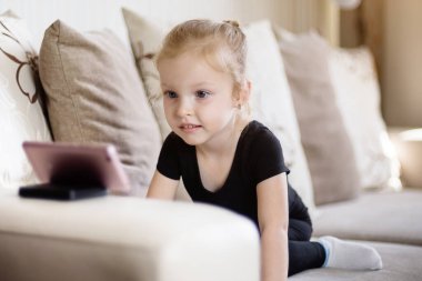 Uzaktan öğrenme, çocuklar için online eğitim. Küçük kız akıllı telefonun önünde evde ders çalışıyor. Çocuk online çizgi film izliyor, çocuk bilgisayar bağımlısı, ebeveyn kontrolü. Evde karantina