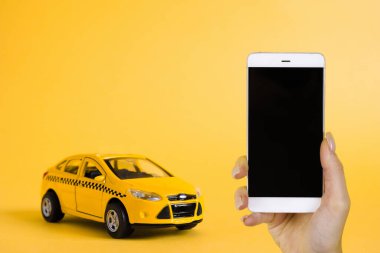 Şehir taksisi mobil online uygulama kavramı. Oyuncak sarı taksi modeli. Vitrinde taksi uygulaması olan akıllı bir telefon. Kopyalama alanı kullan.