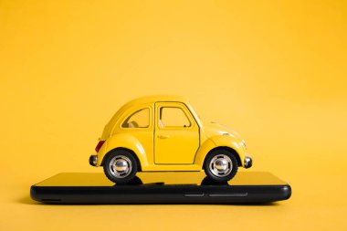 Şehir taksisi mobil online uygulama kavramı. Oyuncak sarı taksi modeli. Vitrinde taksi uygulaması olan akıllı bir telefon. Kopyalama alanı kullan.