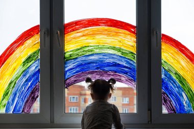 Pencereye gökkuşağı resmi çizen küçük bir kız. Çocuklar evde vakit geçirir. Evde bulunan karantina salgını sırasında olumlu görsel destek Coronavirus Covid-19. 