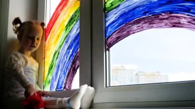 Pencereye gökkuşağı resmi çizen küçük bir kız. Çocuklar evde vakit geçirir. Evde bulunan karantina salgını sırasında olumlu görsel destek Coronavirus Covid-19. 