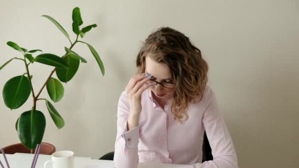 疲倦的女人把头靠在桌子上.坐在办公室的工作位置时头痛的疲倦女人。工作过度的女商人。沮丧的年轻女子紧闭双眼 — 图库视频影像