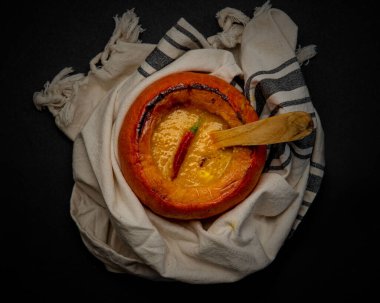 Balkabağı çorbası pişmiş mini balkabağına sarılı beyaz tabak bezine karşı kırmızı biberle süslenmiş ve tepeden izlenmiş, tahta kaşıkla...