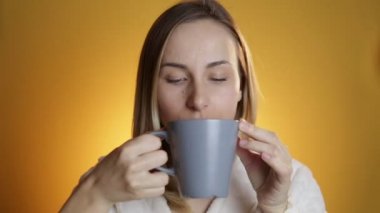 Sarı bir arka plan üzerinde bir kupa çay içme kadın
