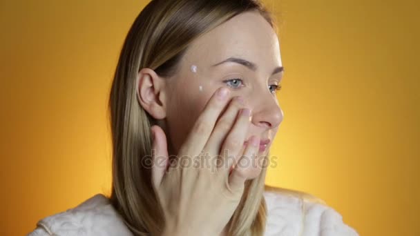 Vrouwelijke schoonheid, gelukkig medio volwassen vrouw crème aanbrengen op gezicht huid en glimlachend, camera kijken. — Stockvideo