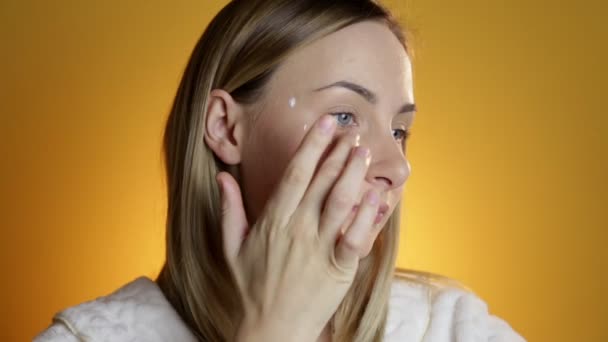 Belleza femenina, mujer adulta media feliz poniendo crema en la piel de la cara y sonriendo, mirando a la cámara . — Vídeo de stock